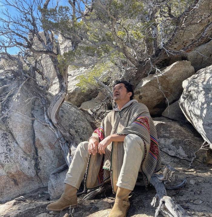 Orlando sits among rocks and looks at the sky in his poncho