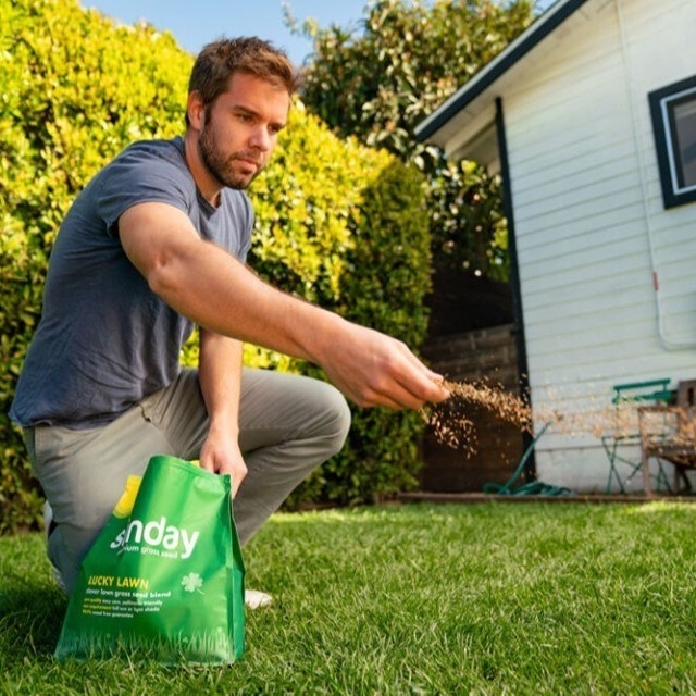 a man bending down reaching into a bag of grass seed