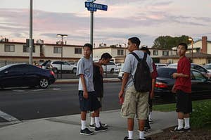 A group of kids stand on a sidewalk corner and look around
