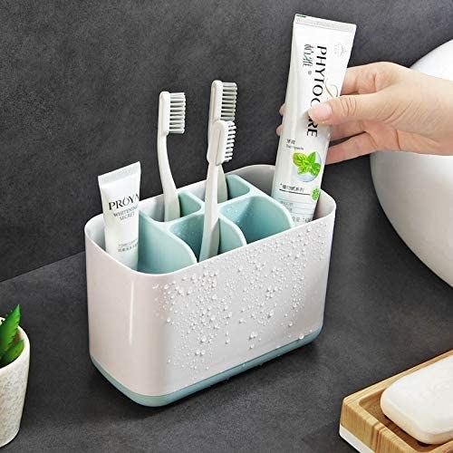A person putting a toothpaste in a toothbrush organiser 