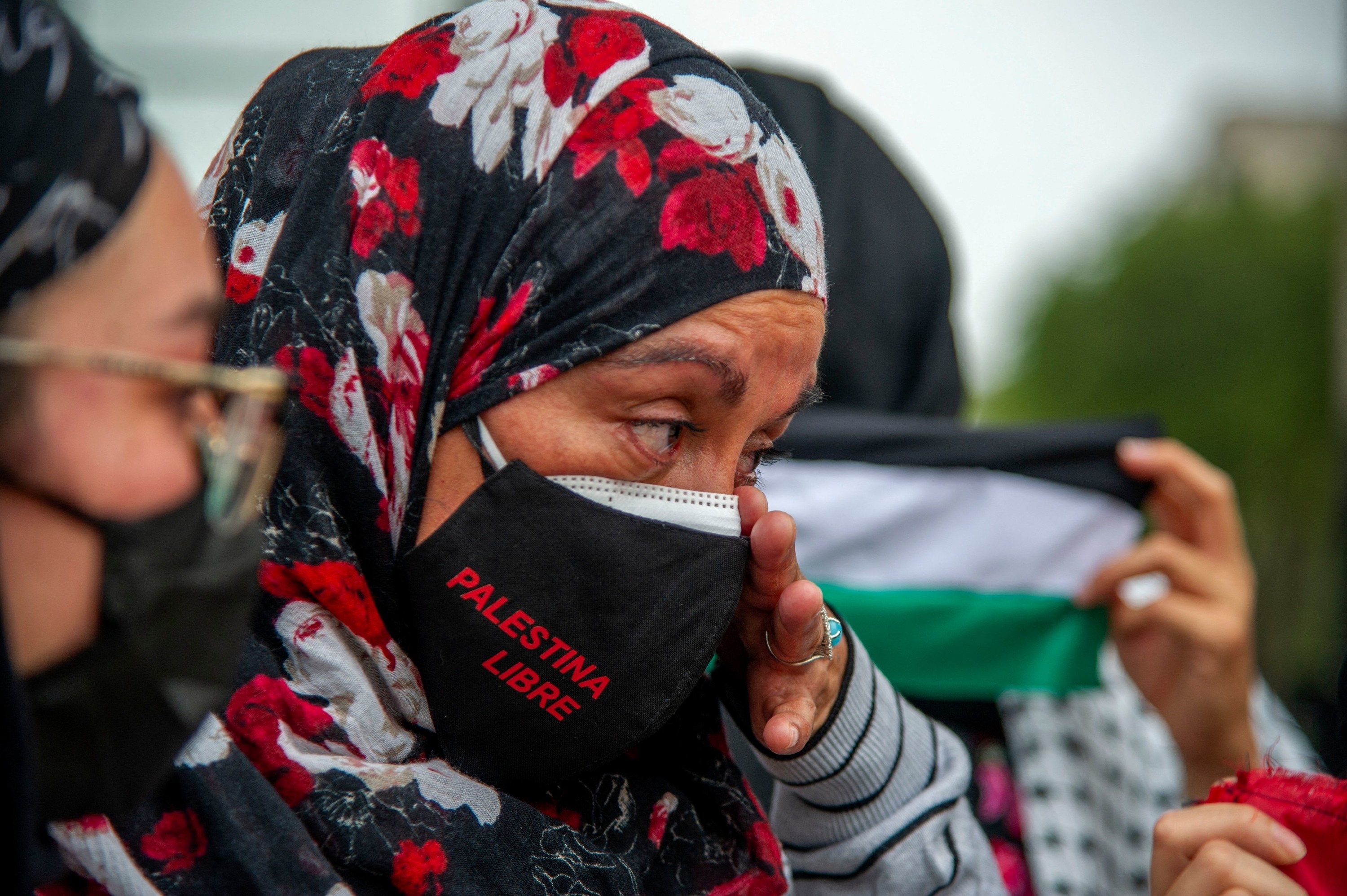 A woman wearing a &quot;Palestina libre&quot; mask wipes a tear from her eye