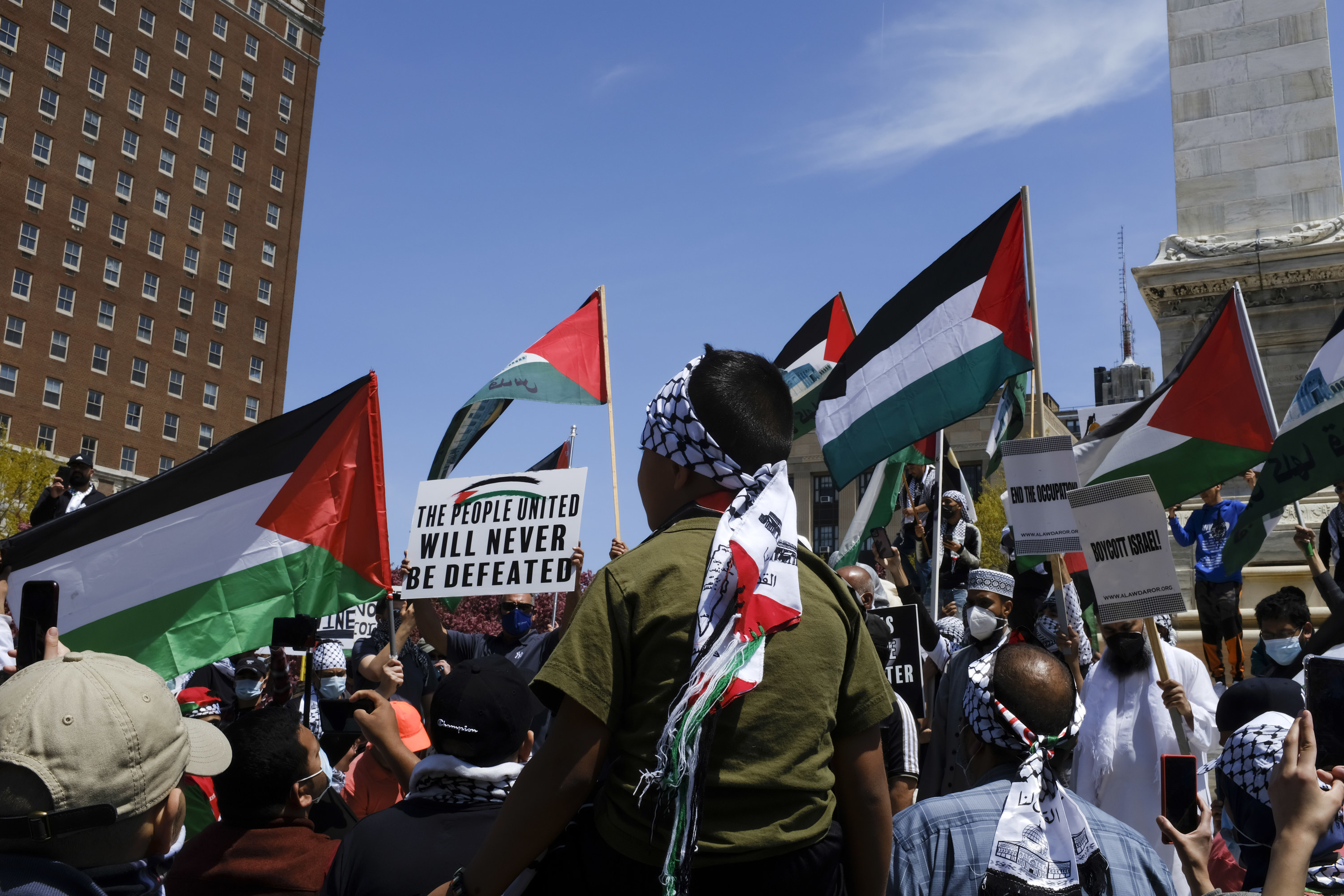 Protesters wave Palestinian flags and a sign reading, &quot;The people united will never be defeated&quot;