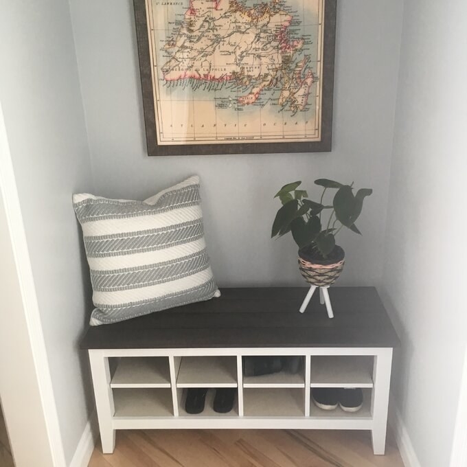 The bench holding shoes in a reviewer&#x27;s home with a pillow and a plant on top 