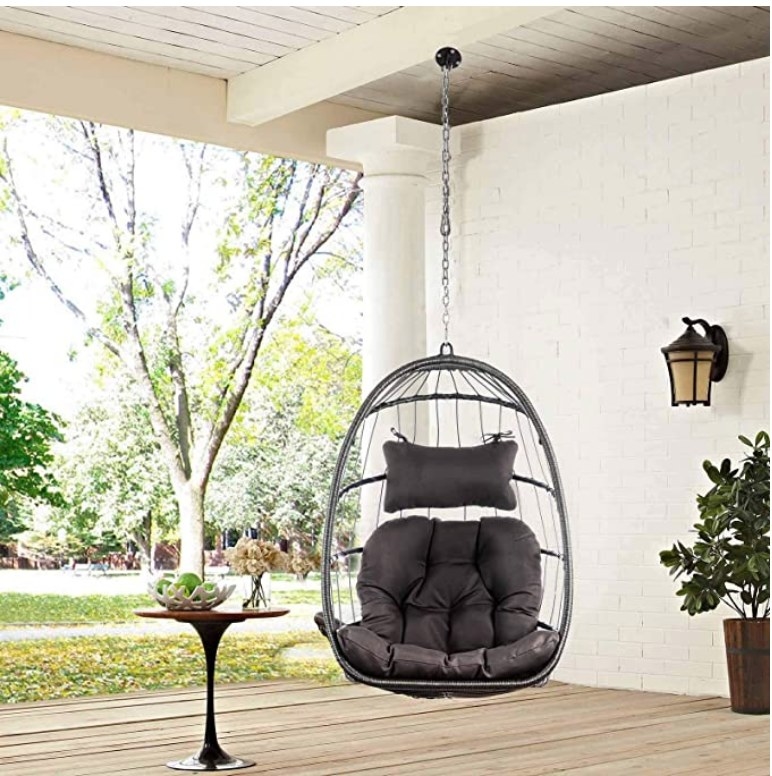 A charcoal, hanging, egg chair hammock, hanging from the ceiling of a patio