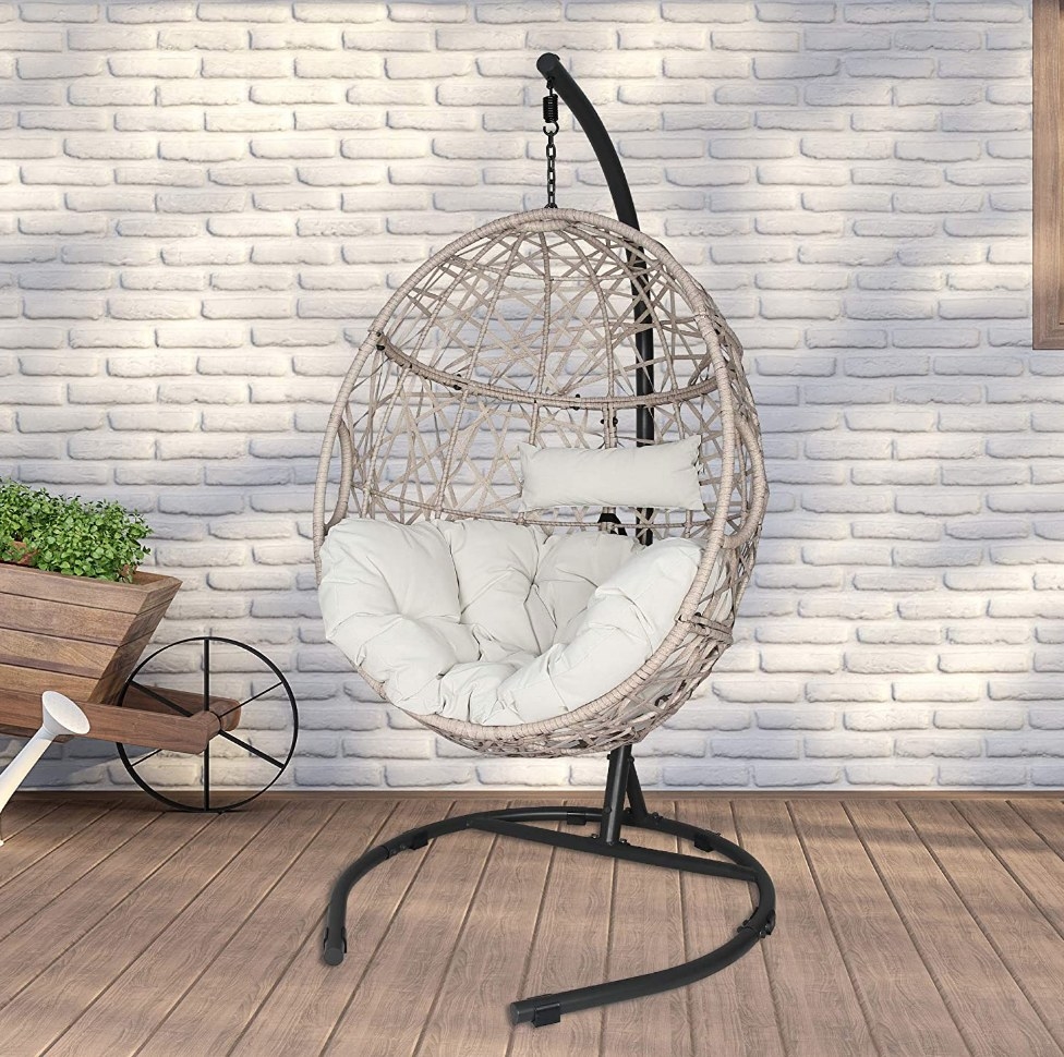A beige, outdoor, wicker egg hammock on a stand with cushions