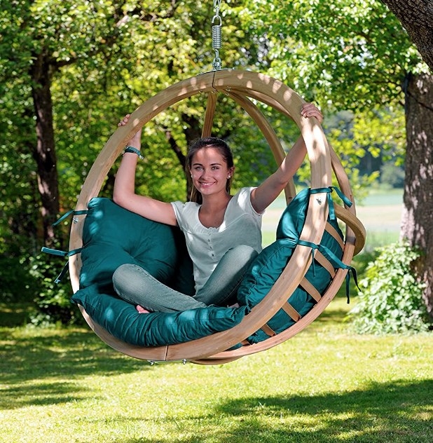 A model inside a wooden, hanging hammock with green cushions hanging from a tree