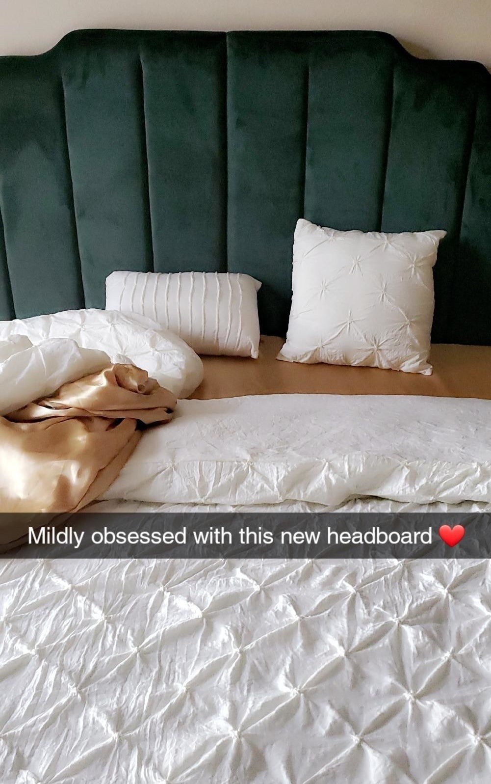 a reviewer photo of their velvet headboard in a deep green that has text written over it that reads mildly obsessed with this new headboard