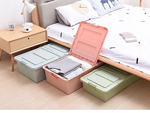 A set of three boxes in grey, pale pink and pale green pictured halfway under a bed.
