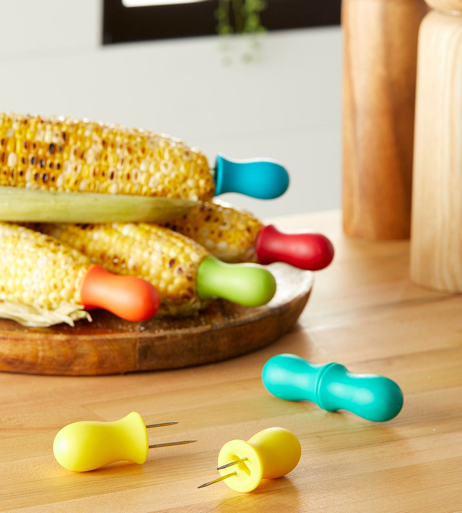 A set of colourful corn cob holders attached to grilled cobs