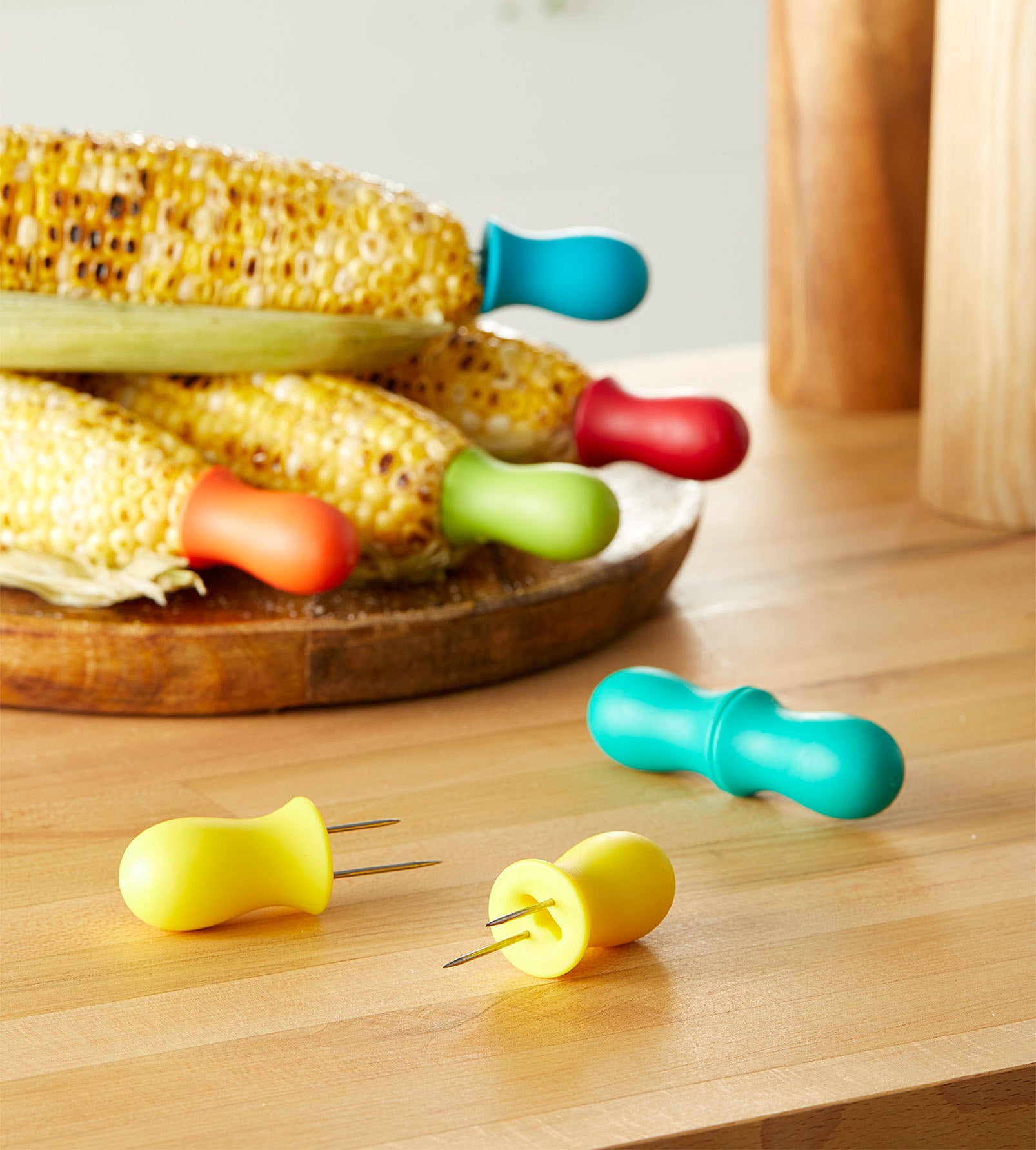 A set of colourful corn cob holders attached to grilled cobs