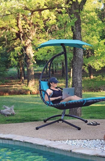 a reviewer sitting in a blue swing using a laptop