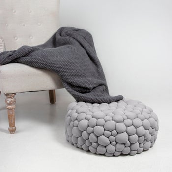 A. bubbly floor pillow on a the floor next to couch and blanket