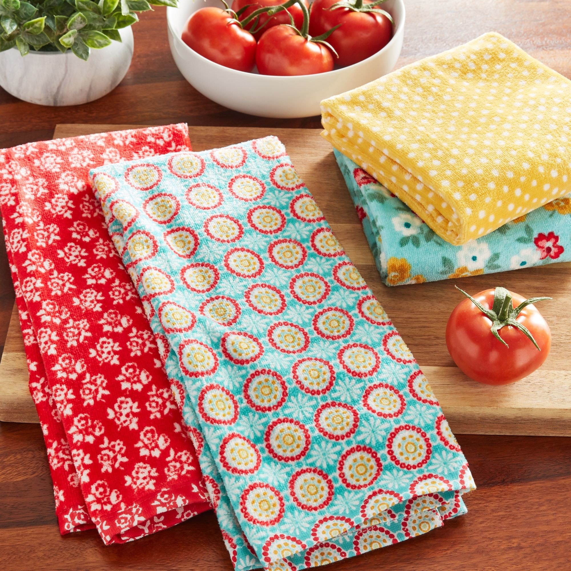 the kitchen towel set with one red and white towel, one yellow with polka dots, and one blue with a red and yellow flower pattern