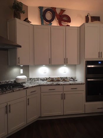 a reviewer photo of the under cabinet lights shining underneath kitchen cabinets