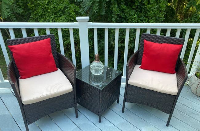a reviewer photo of two rattan arm chairs with a matching side table with a glass top 