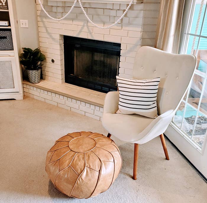 Reviewer&#x27;s light brown leather pouf is styled in a room.