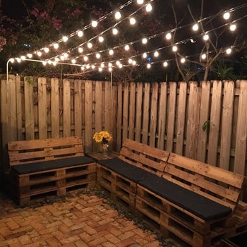 a reviewer photo of a backyard with strings of lights handing above a set of benches 