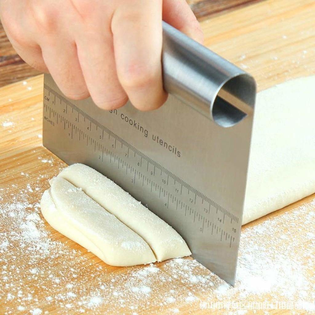 A steel bench scraper with measurements being used to cut dough