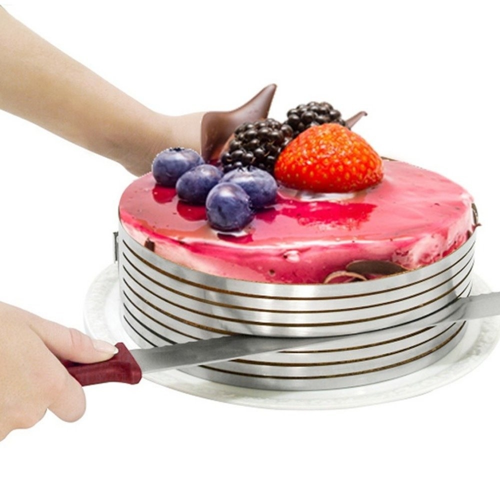Round steel cake slicer with cake inside, being cut by a knife through one of the slicer&#x27;s guides