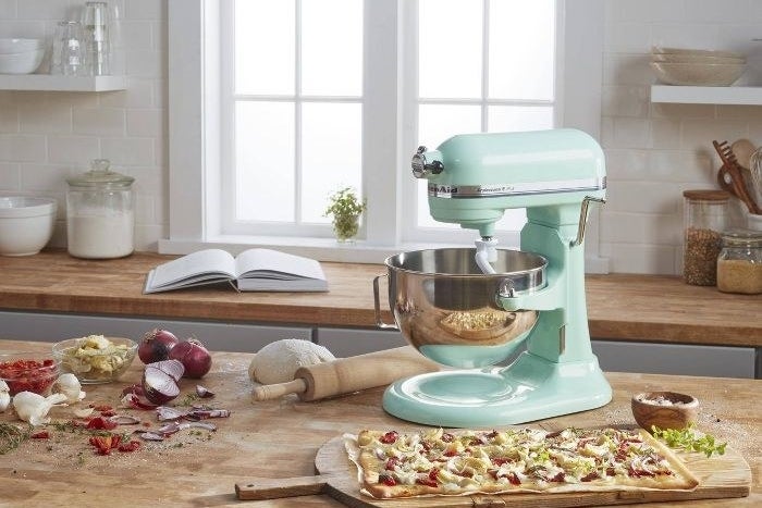 The mixer in ice blue in a kitchen with a pizza and ingredients nearby, implying it was just used to make a pizza