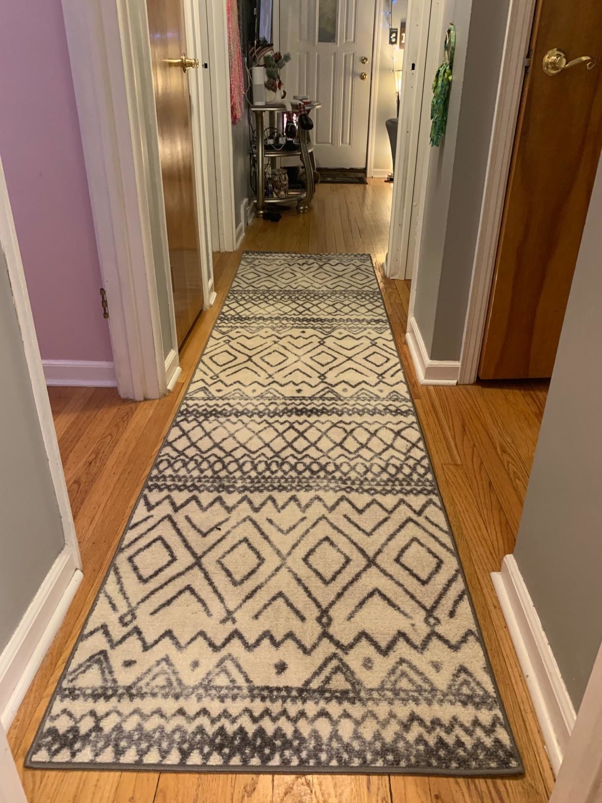 a reviewer photo of the carpet runner in a hallway in a neutral beige with a dark colored pattern