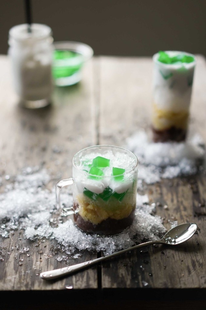 Glass cup containing three layers of (from top): crushed ice mixed with coconut cream and jelly pieces, mung beans, and red beans