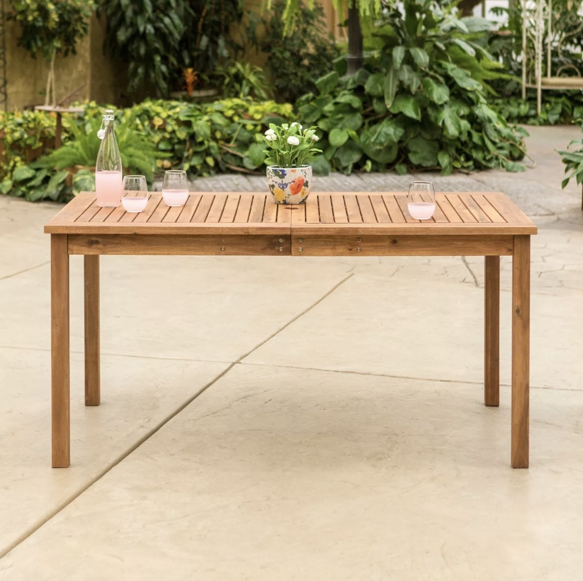 A long light brown table with a slatted top in a lush outdoor setting