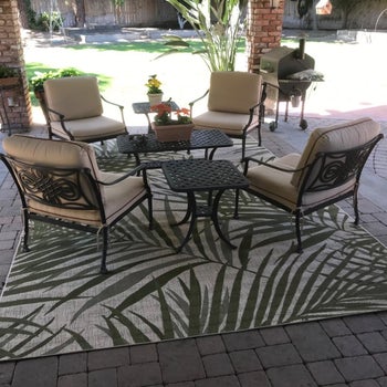 a reviewer photo of four chairs around a table on a patio overtop a rug with a palm print 