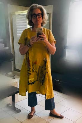 short sleeve yellow dress with embroidered flowers. the reviewer is wearing the dress with flared jeans and flats.