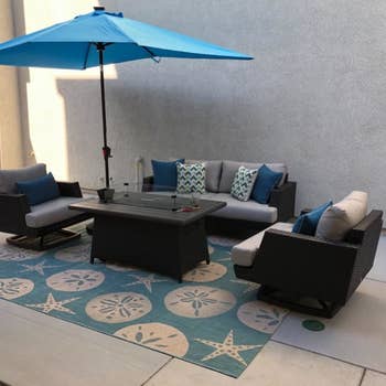 a reviewer photo of a patio couch and chairs set atop a blue outdoor rug with a shell print 