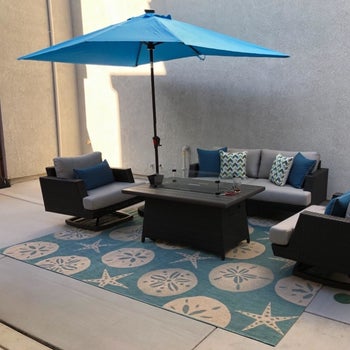 a reviewer photo of a patio couch and chairs set atop a blue outdoor rug with a shell print 
