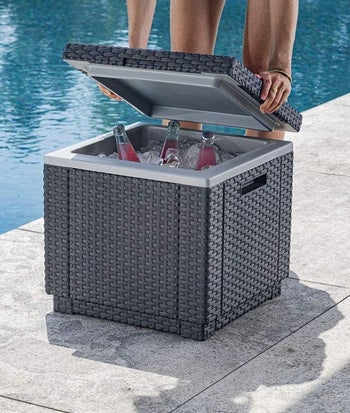 a model placing a lid on the woven cube ottoman with ice and bottles inside 