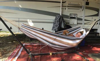 a reviewer of a freestanding hammock on a stand with someone inside with a small dog 