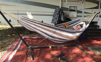a reviewer of a freestanding hammock on a stand with someone inside with a small dog 
