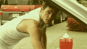 A man in a sleeveless shirt working on a car