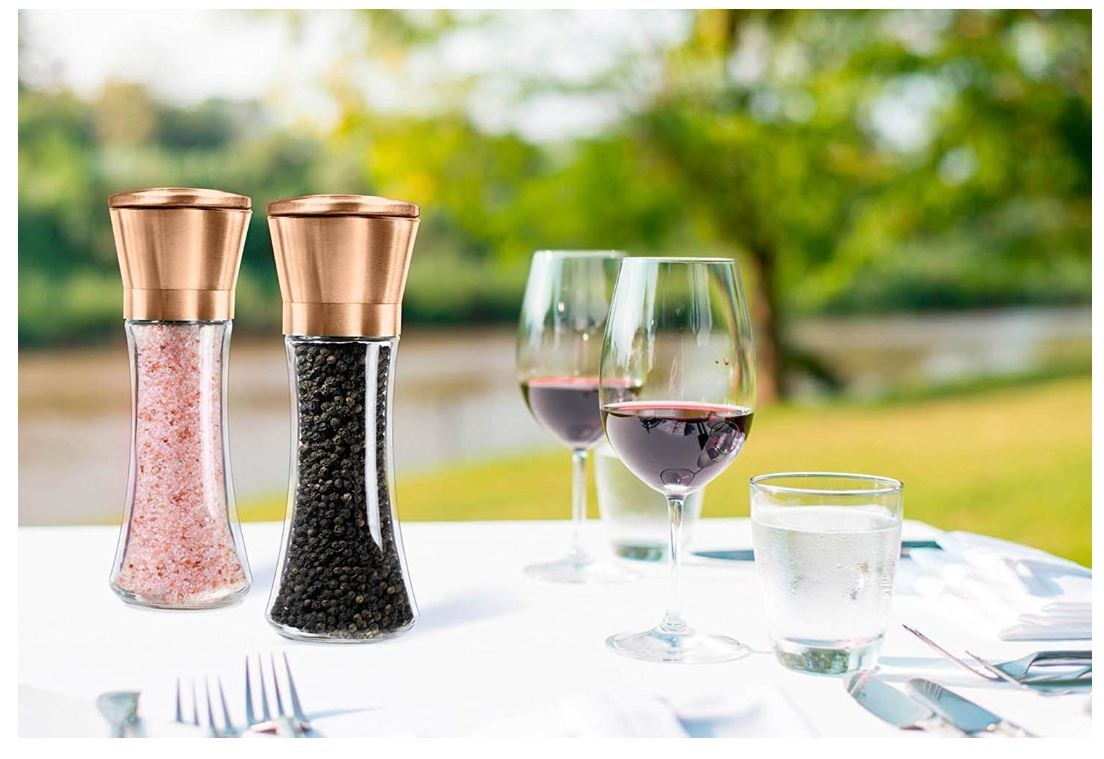 the salt and pepper grinders with copper tops next to two glasses of red wine