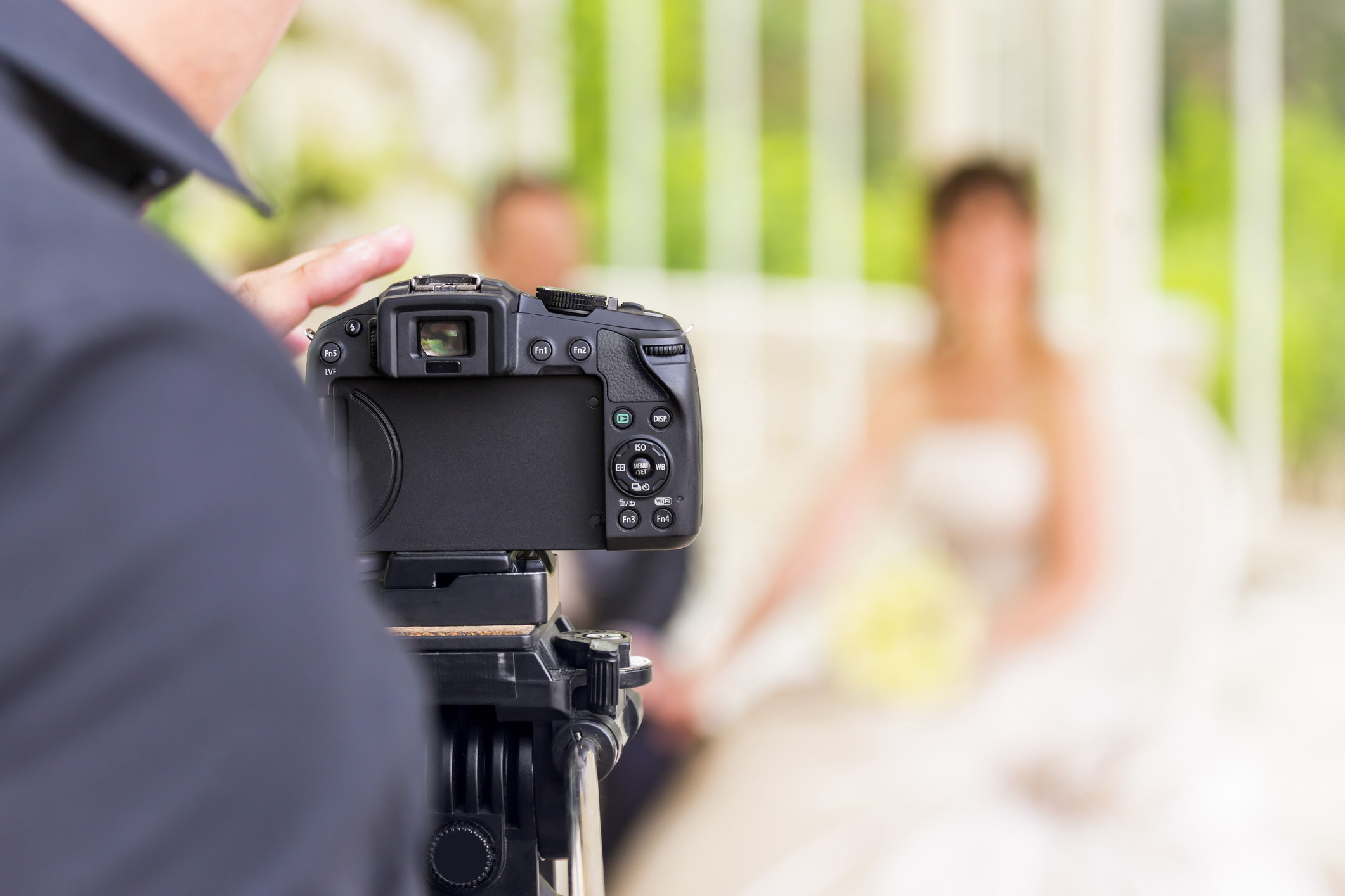 Close-up of the back of a camera, with a fuzzy image of a bride and groom in the backgkround
