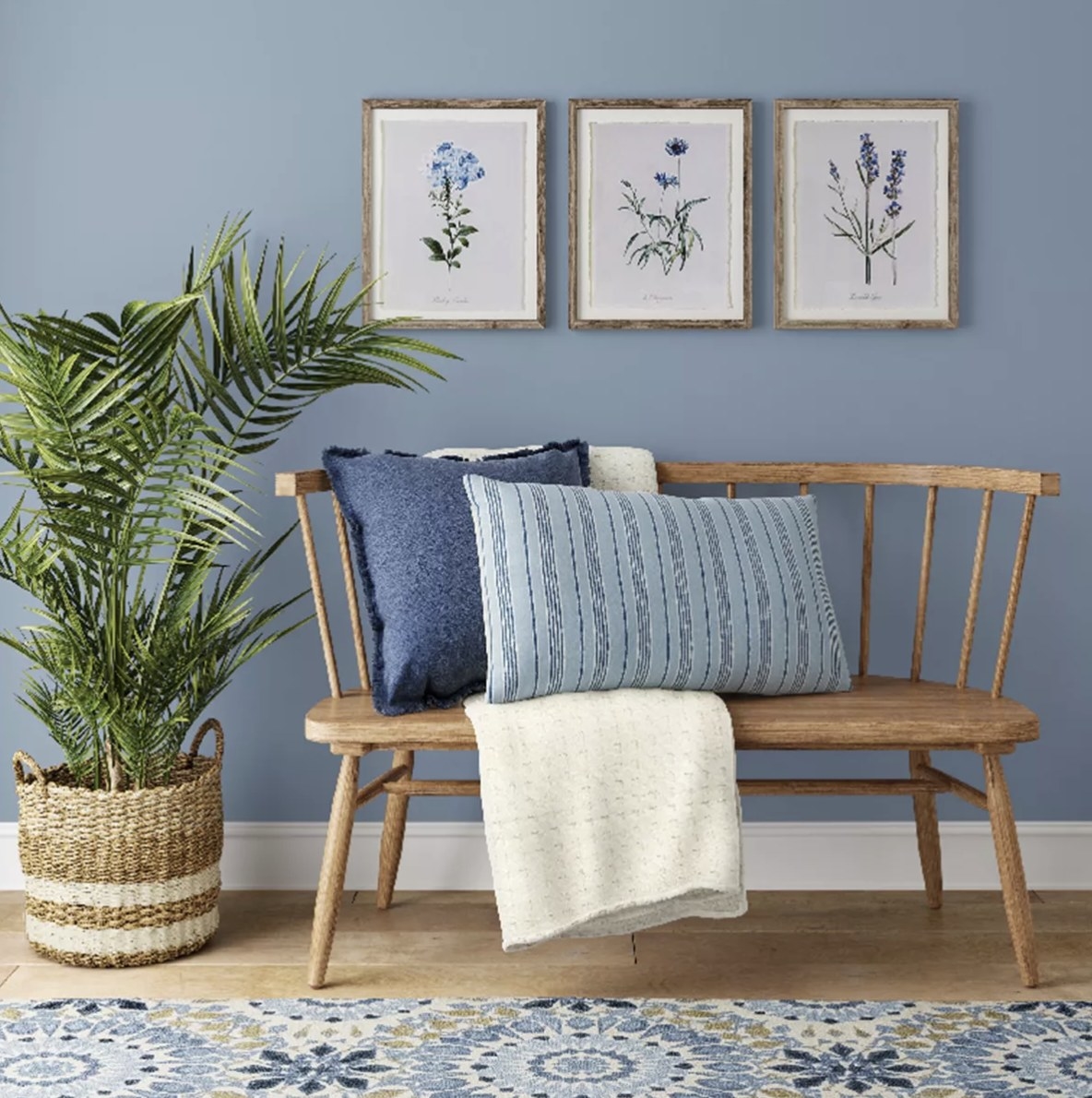 The set of three flower prints is hung on a blue wall and surrounded by rustic furniture