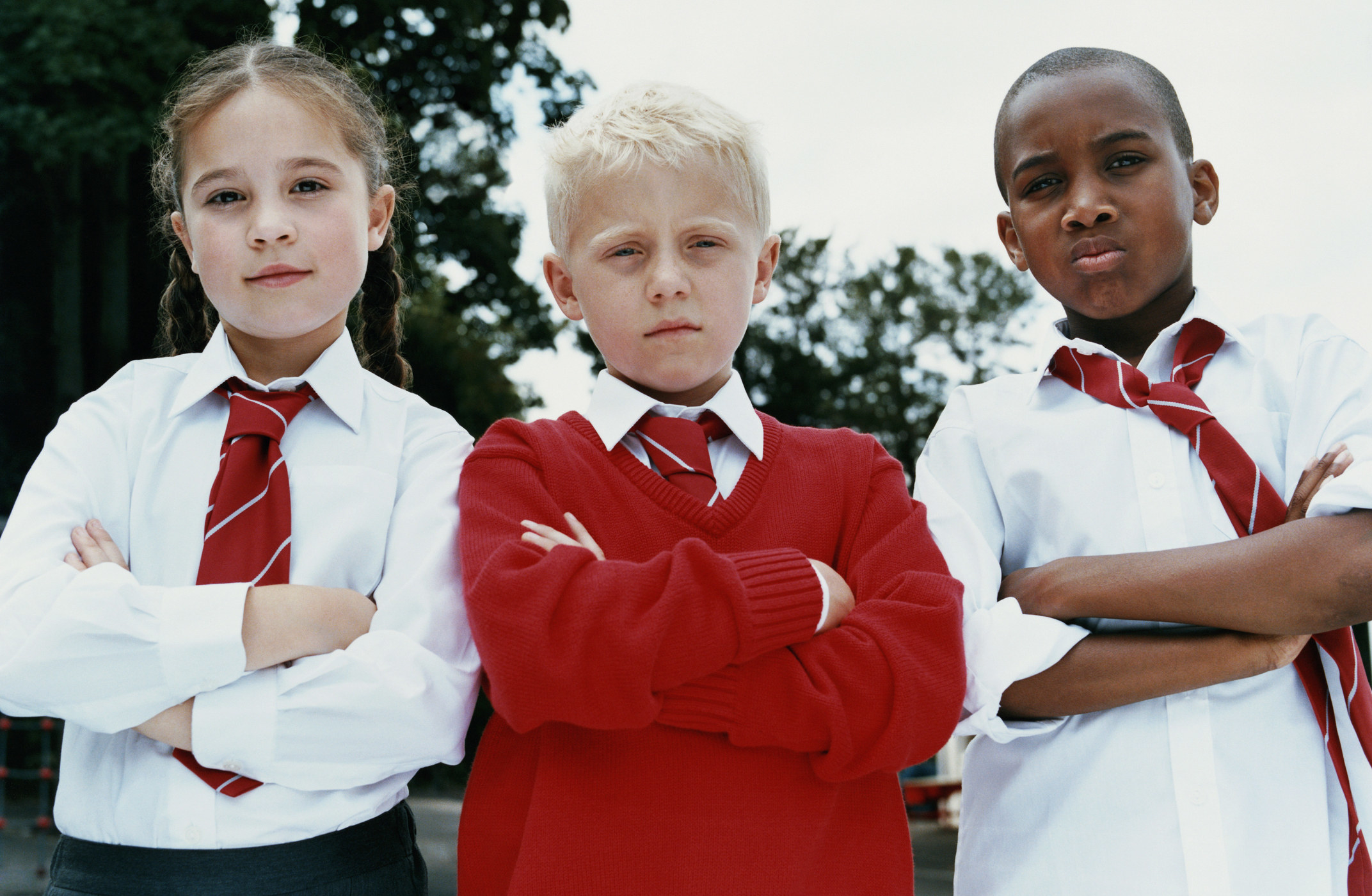 Portrait of three primary school children standing with their arms folded, scowling at the camera and wearing uniforms with ties