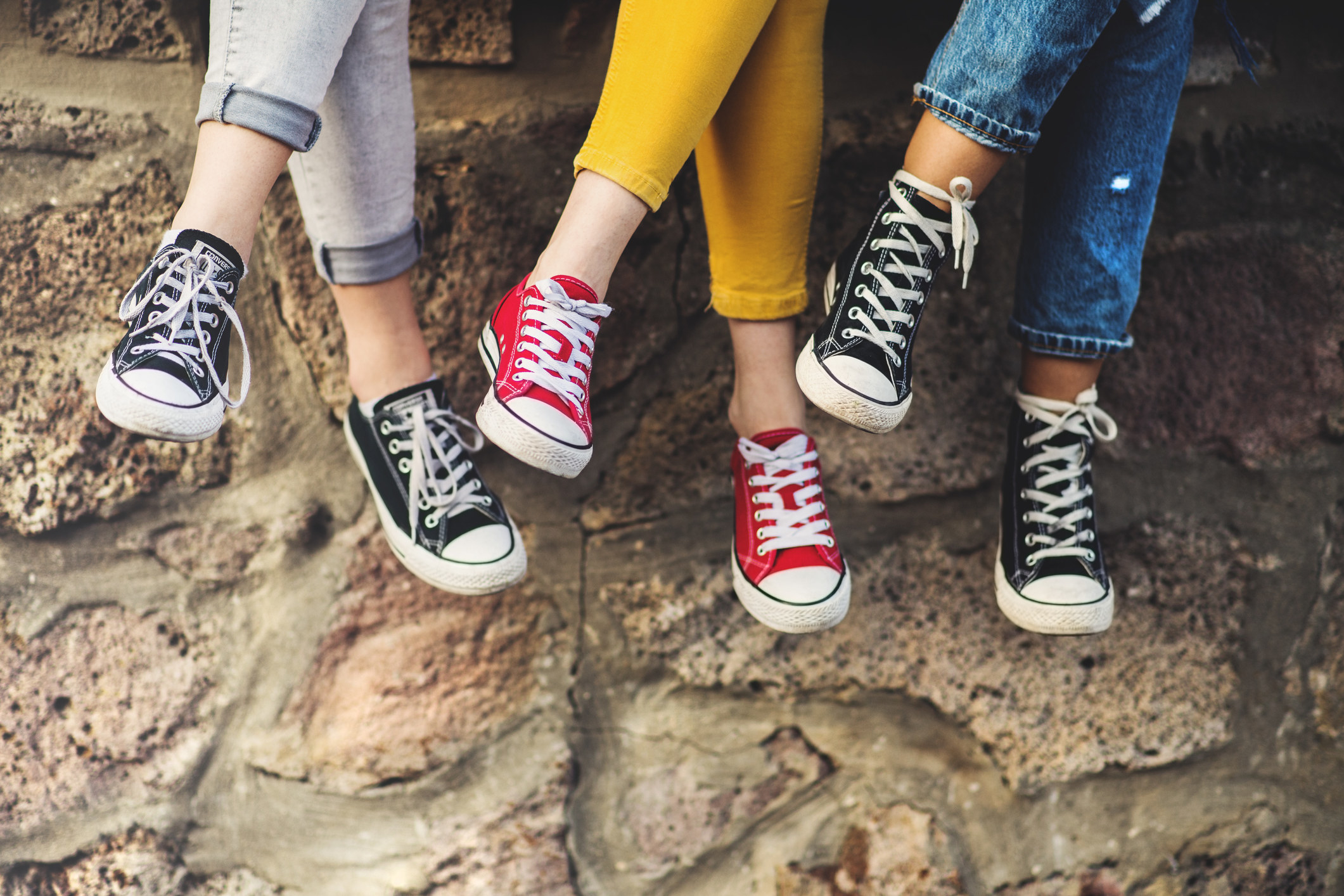 Legs of three female teenager friends sitting cross-legged on a wall, wearing sneakers