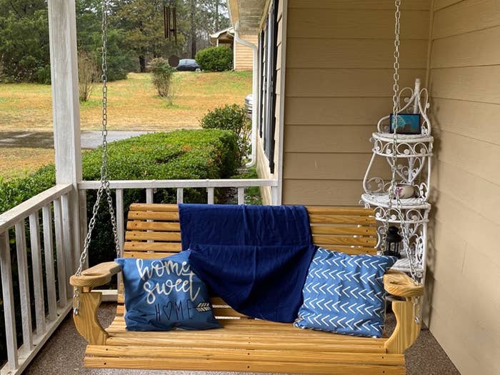 a reviewer photo of their porch swing and the decorative pillows on the swing the pillows are blue and one reads home sweet home and the other is patterned 