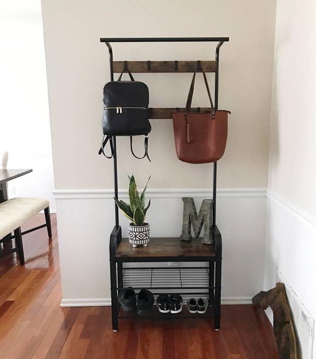 a reviewer photo of their entry way organizer with shoes on the bottom a couple of purses hanging from the hooks at the top and a plant and decorative letter M sitting on the shelf