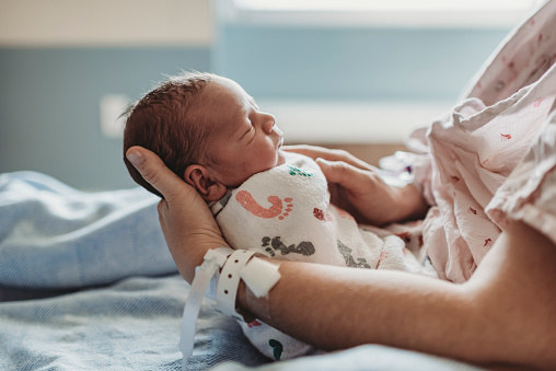 A woman holds her newborn baby in a hospital bed.