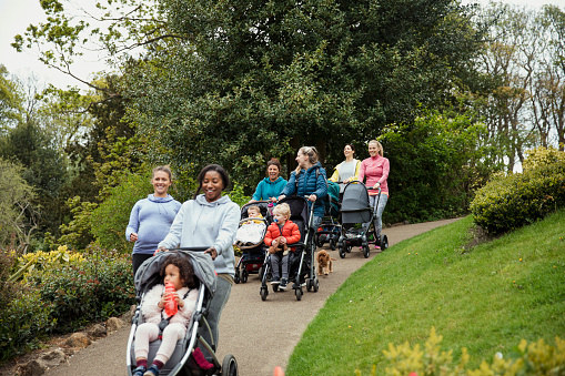 A group of happy mums and their children walk in the park together.