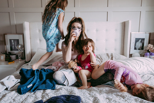 An overwhelmed mum sits on her bed surrounded by children and mess.