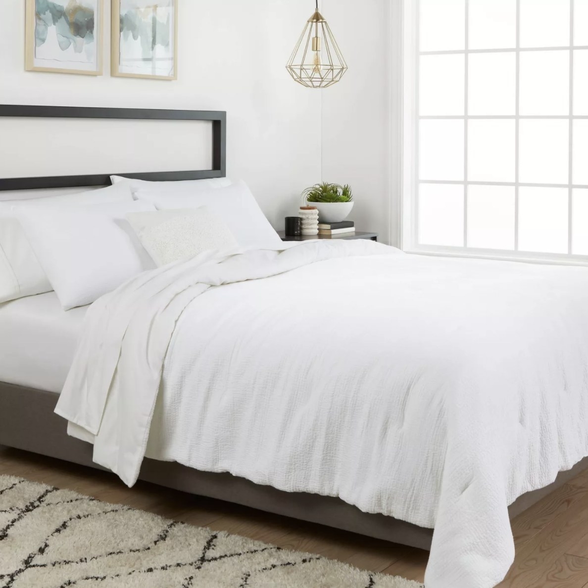 A bright white textured comforter on a black and brown bed frame in a well lit room