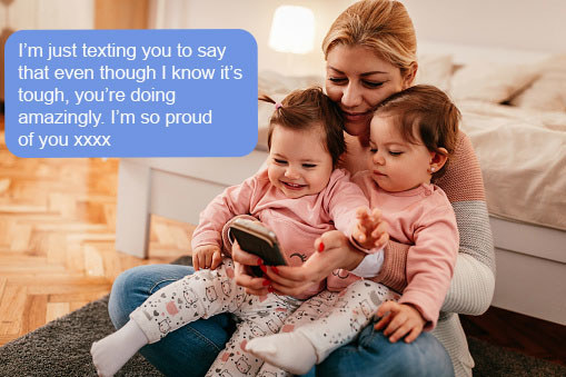 A woman with two babies in her lap is looking on her phone. She is reading a text which says, &quot;I&#x27;m just texting you to say that even though I know it&#x27;s tough, you&#x27;re doing amazingly. I&#x27;m so proud of you xxxx&quot;
