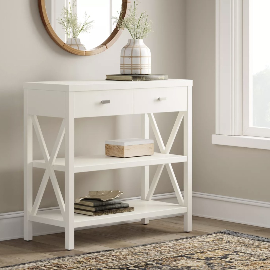 A white consol table with X-sides, two shelves and two drawers