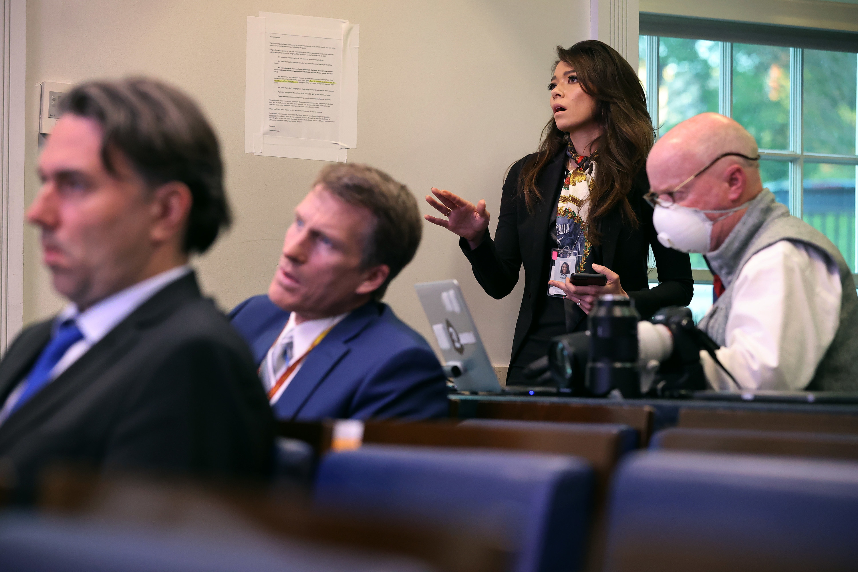 A news reporter stands and asks a question to someone out of frame