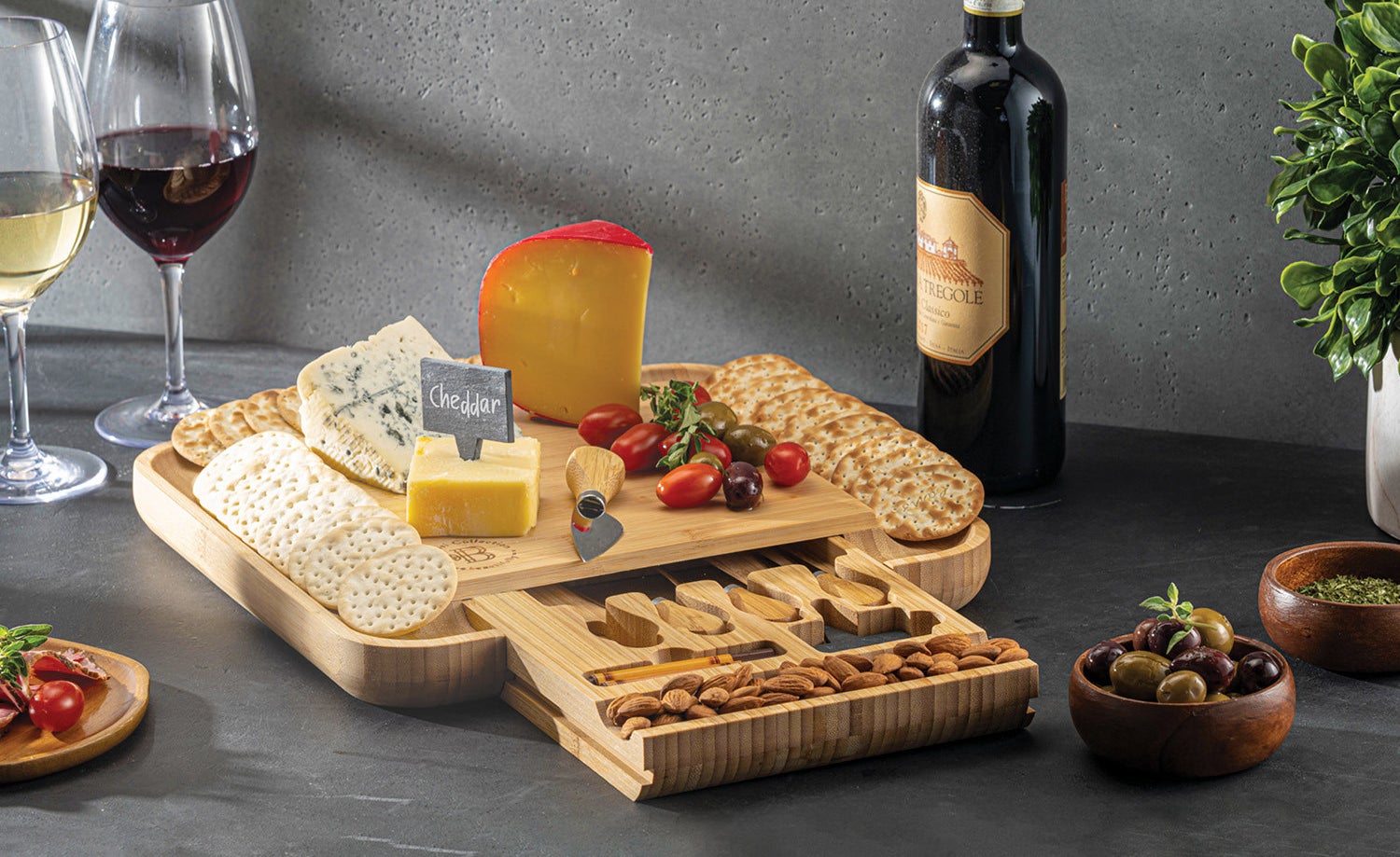 the cheeseboard with cheese, fruits, and crackers on it and wine next to it